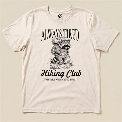 The "Always Tired Club Shirt" features a raccoon with a backpack and the slogan "Why Are We Doing This?" on a graphic t-shirt.