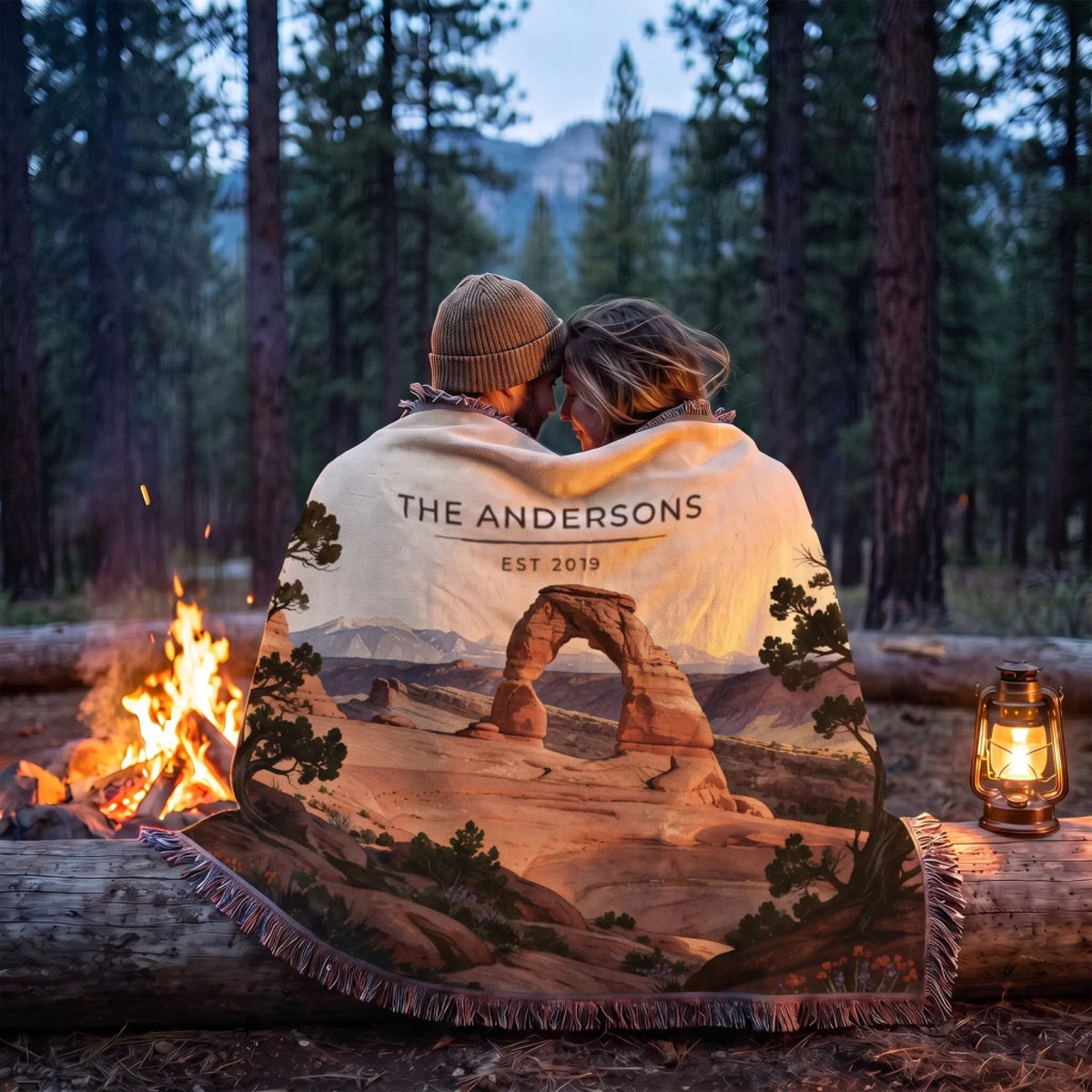 Couple wrapped in the Arches Delicate Arch Sunset Woven Blanket by a campfire