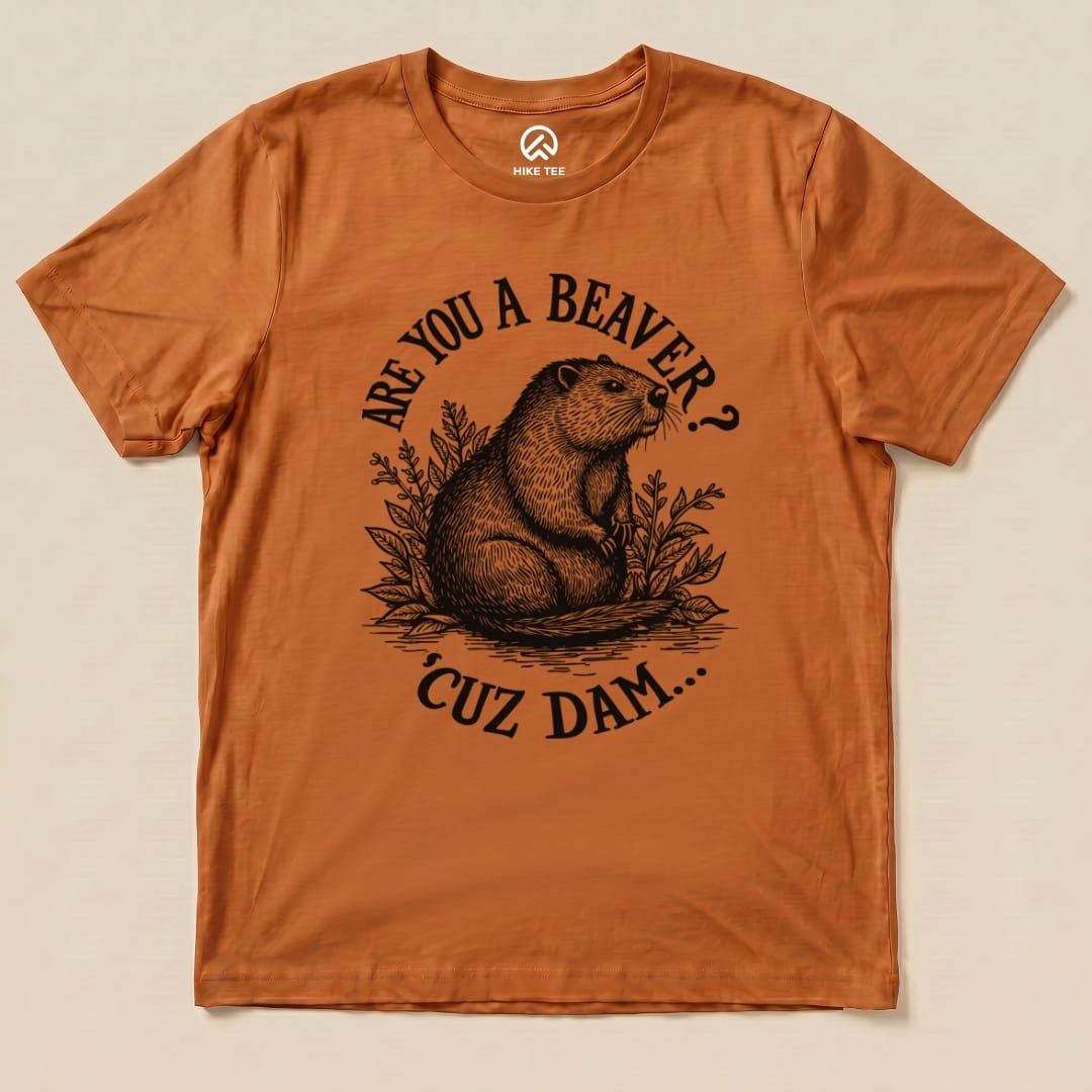 A graphic t-shirt in burnt orange featuring the slogan "Are U A Beaver? Cuz Dam..." with an illustrated beaver and foliage design.
