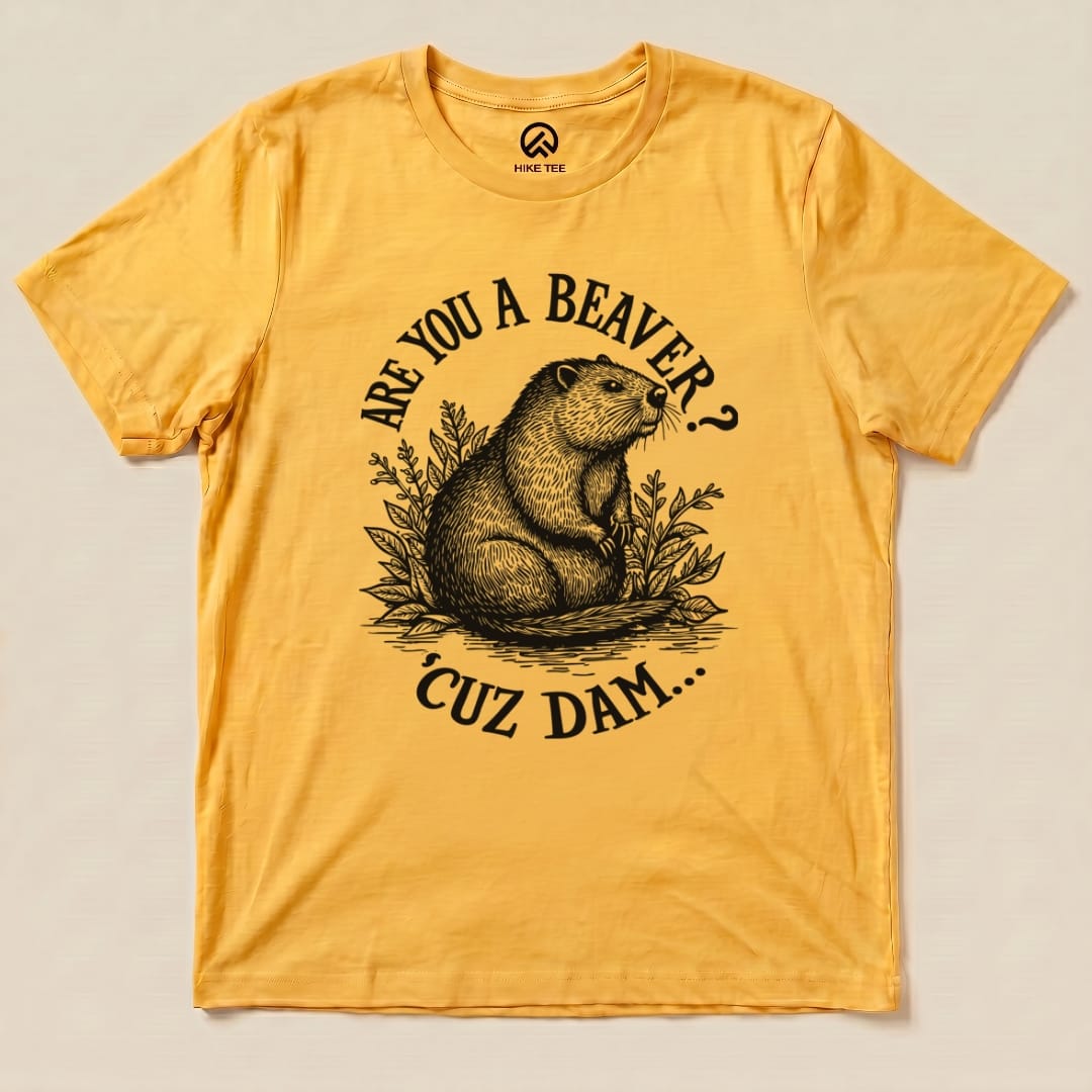 A graphic t-shirt in vibrant yellow featuring the text "Are U A Beaver? Cuz Dam..." alongside an illustration of a beaver surrounded by foliage.