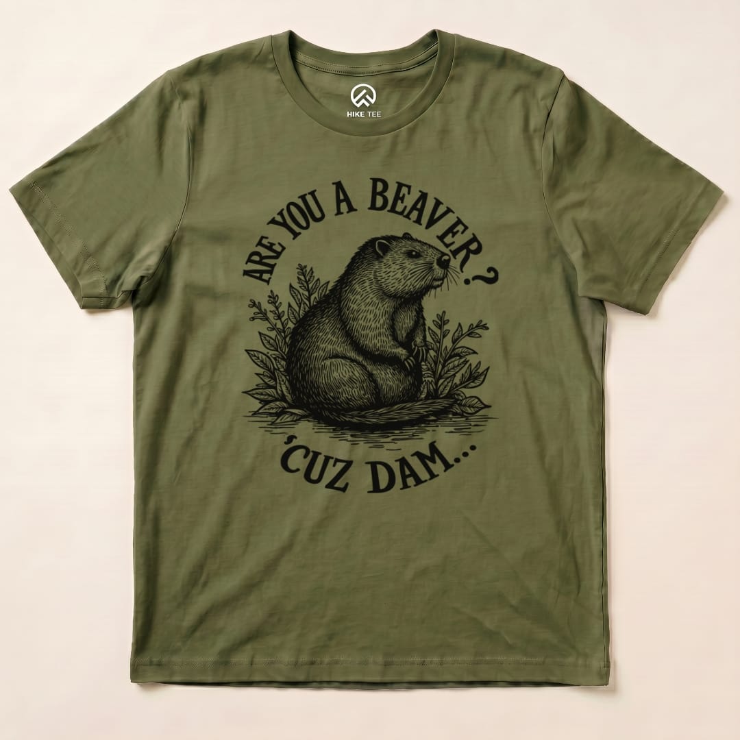 Graphic t-shirt in olive green featuring a beaver surrounded by foliage, with the humorous text "Are U A Beaver? Cuz Dam..." printed prominently.