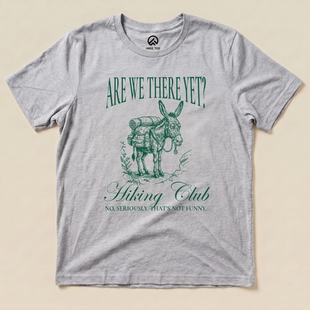 A gray graphic t-shirt featuring a donkey with a backpack and the slogan "Are We There Yet? Hiking Club" beneath it.