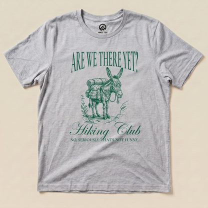 A gray graphic t-shirt featuring a donkey with a backpack and the slogan "Are We There Yet? Hiking Club" beneath it.