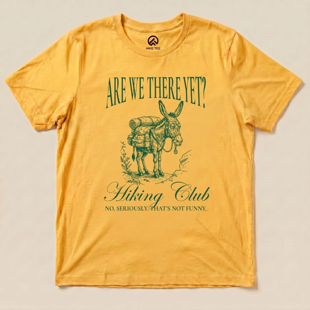 Yellow graphic t-shirt featuring a donkey with a backpack, reading "Are We There Yet? Hiking Club - No, seriously, that's not funny.