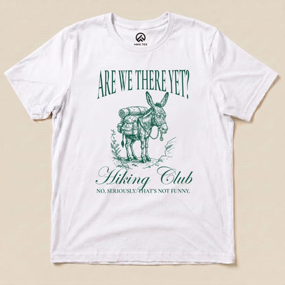 A white graphic t-shirt features a cartoon donkey with a backpack, showcasing the slogan "Are We There Yet? Hiking Club" and "No, seriously. That's not funny.
