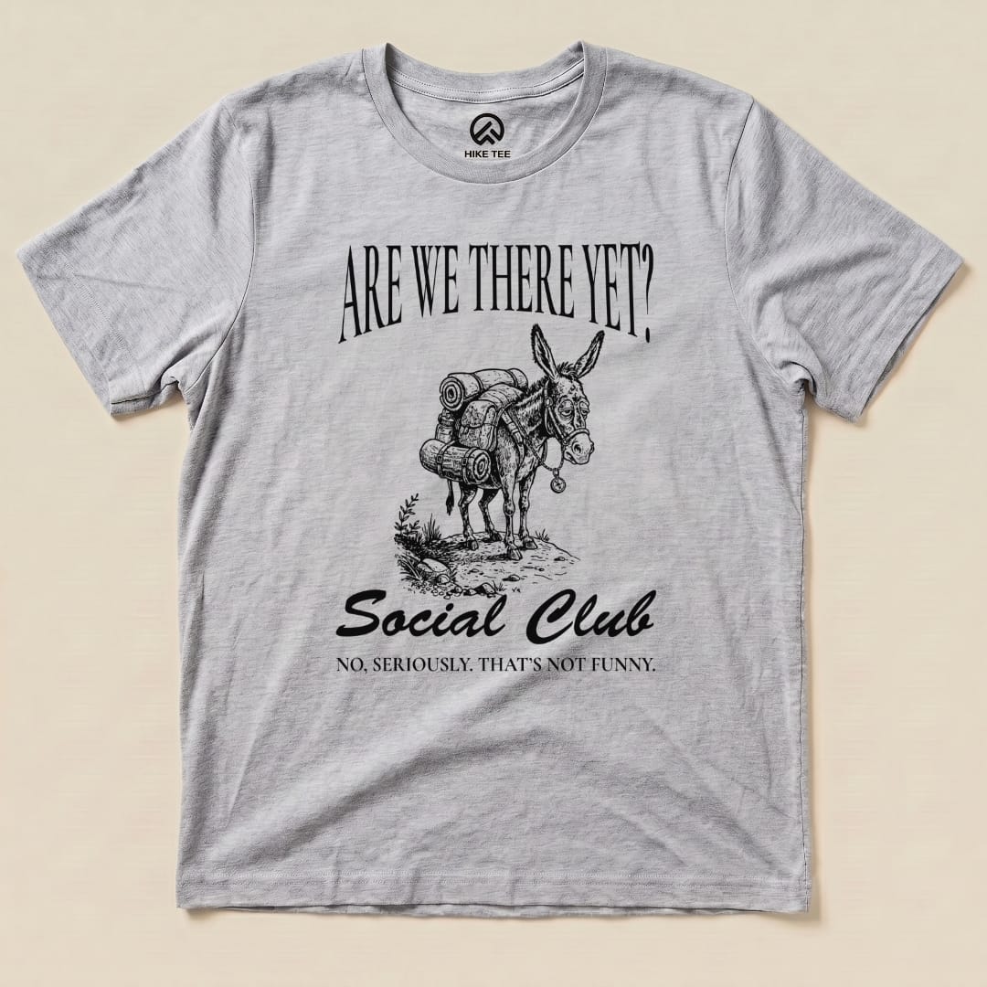 A graphic t-shirt featuring a donkey with a backpack, printed with "Are We There Yet? Social Club" and a humorous tagline below.
