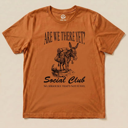 Brown graphic t-shirt featuring the slogan "ARE WE THERE YET? Social Club" with a humorous illustration of a donkey carrying hiking gear.