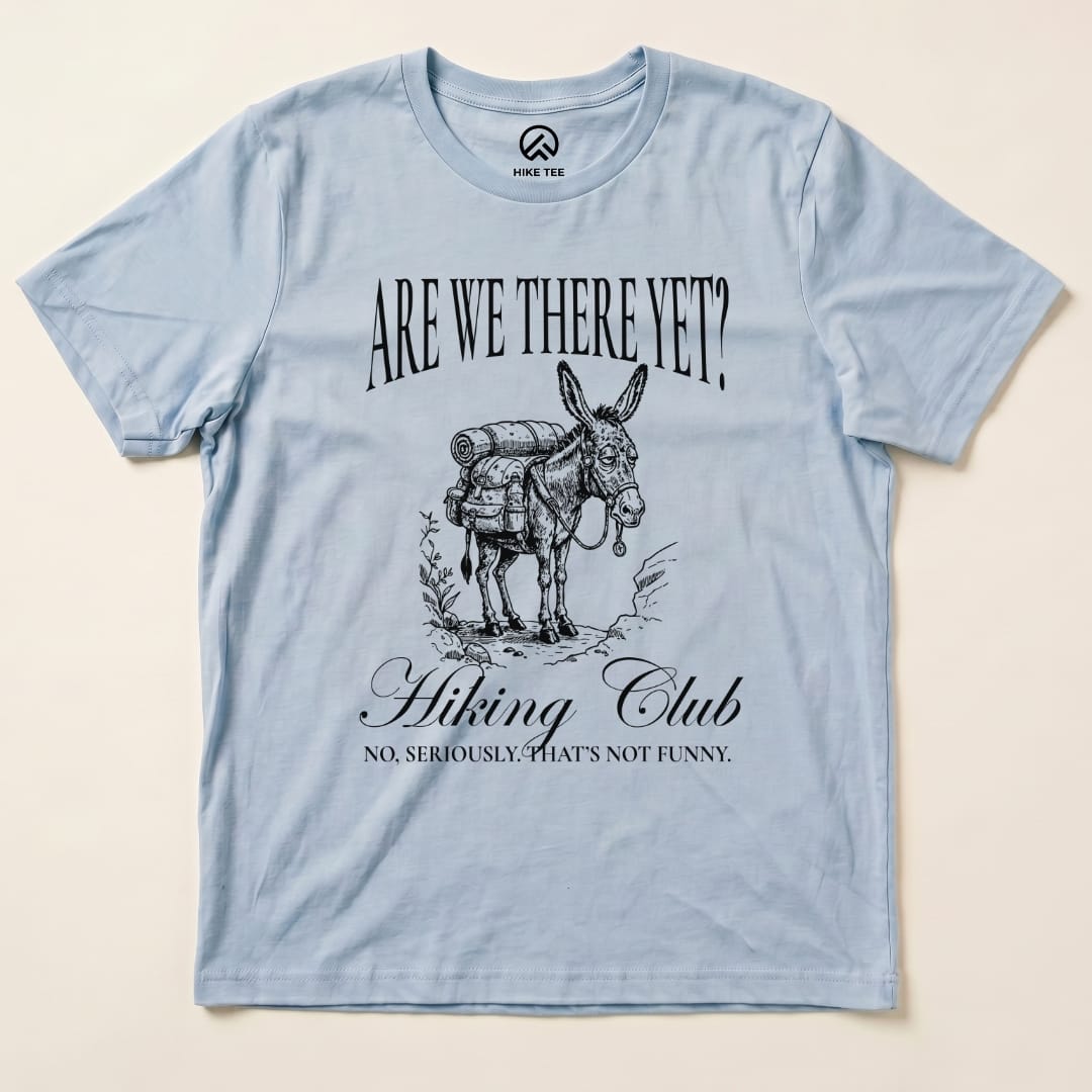 A light blue graphic t-shirt featuring a donkey with a backpack and the words "Are We There Yet? Hiking Club" printed above and below.