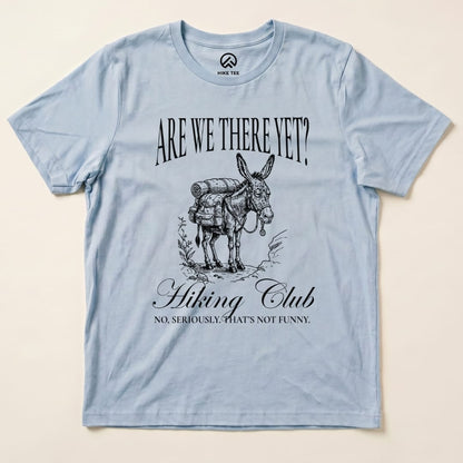 A light blue graphic t-shirt featuring a donkey with a backpack and the words "Are We There Yet? Hiking Club" printed above and below.