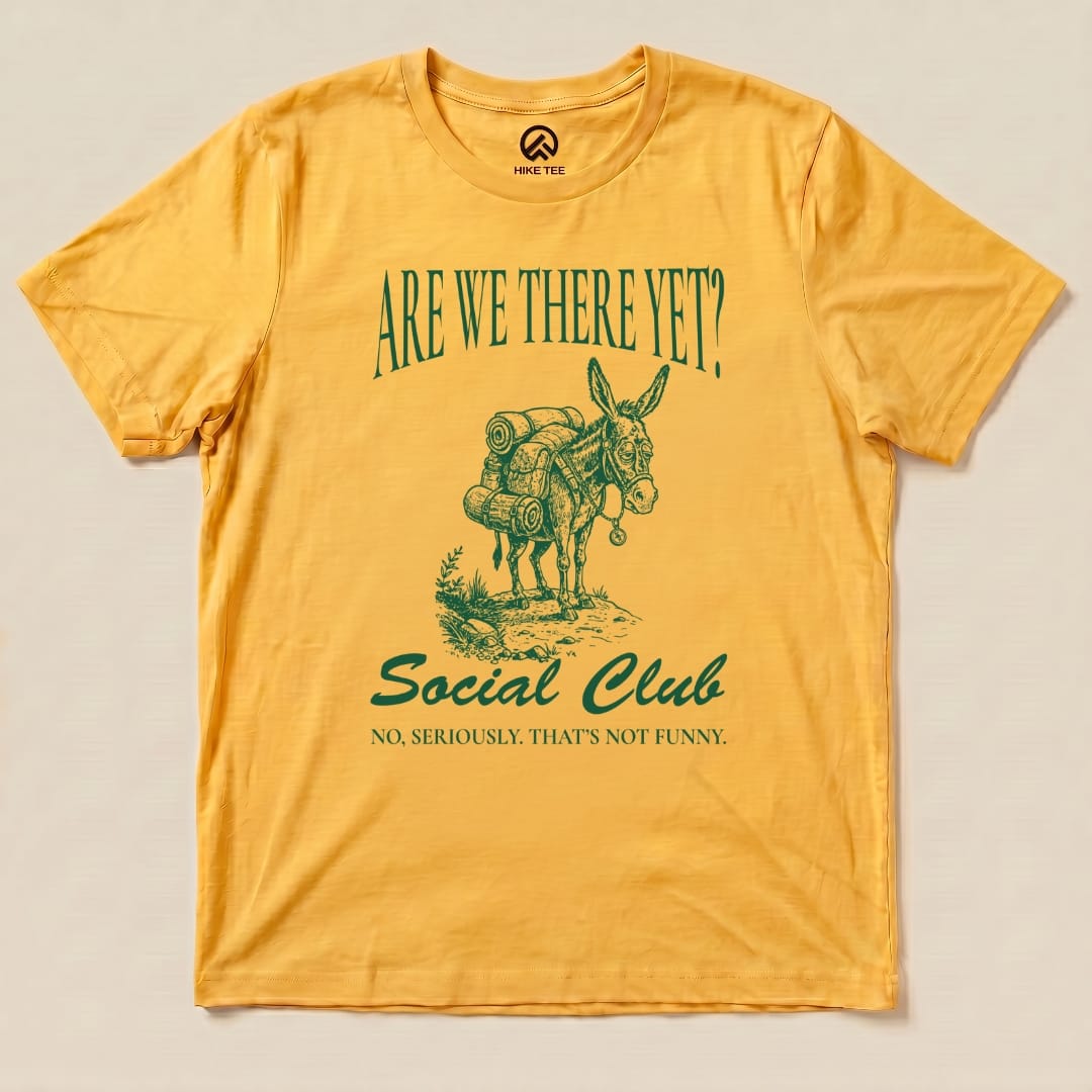 A yellow graphic t-shirt features a donkey with a backpack and the text "Are We There Yet? Social Club" above and a slogan below.