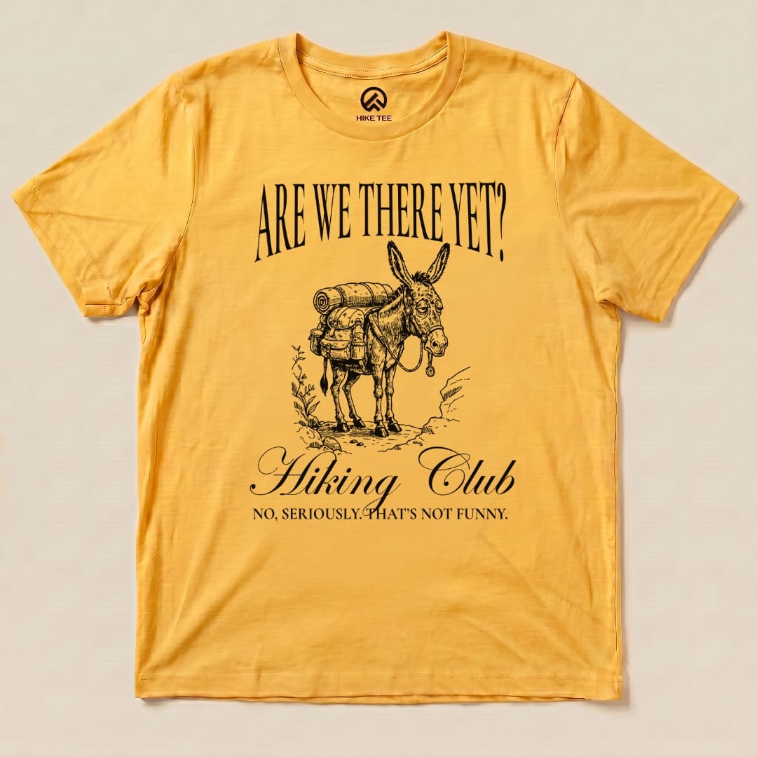 A yellow graphic t-shirt with the slogan "Are We There Yet? Hiking Club" and an illustration of a donkey carrying a backpack.