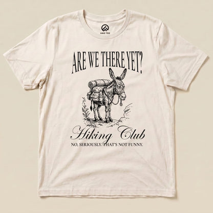 A flat view of the "Are We There Yet? Club Shirt" featuring a donkey with a backpack and the slogan "No, seriously. That's not funny.