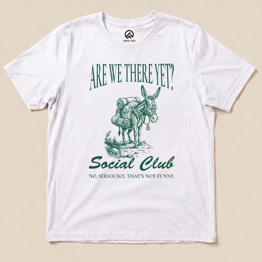 A white graphic t-shirt features an illustration of a donkey with backpacks and the text "Are We There Yet? Social Club" and "No, seriously. That’s not funny.