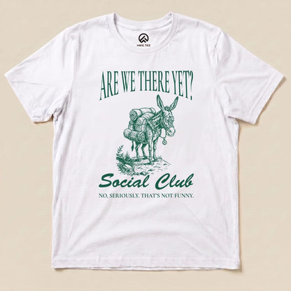 A white graphic t-shirt features an illustration of a donkey with backpacks and the text "Are We There Yet? Social Club" and "No, seriously. That’s not funny.