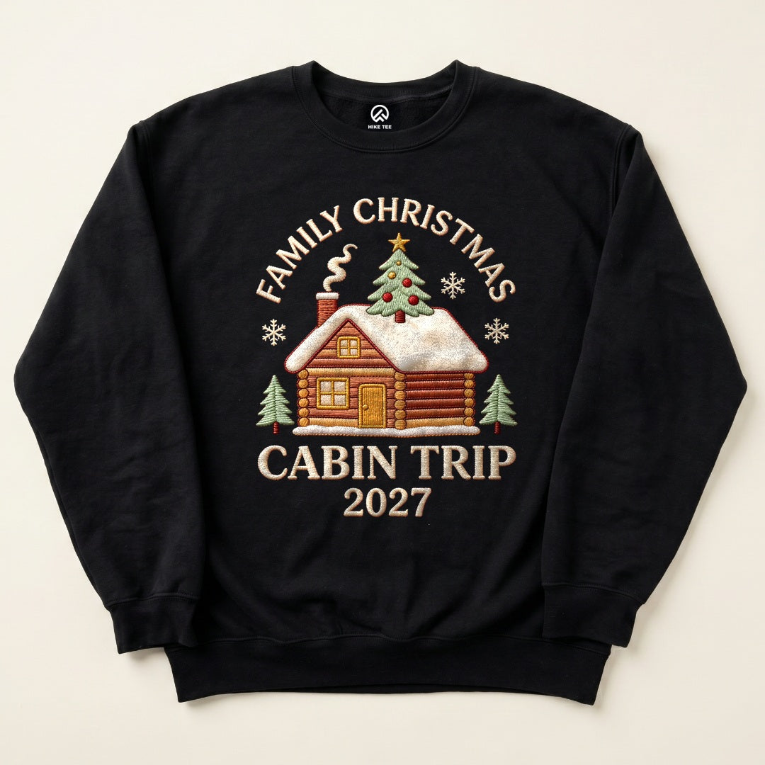 Black Family Christmas Cabin Trip 2027 Sweatshirt with a snowy log cabin and Christmas tree graphic