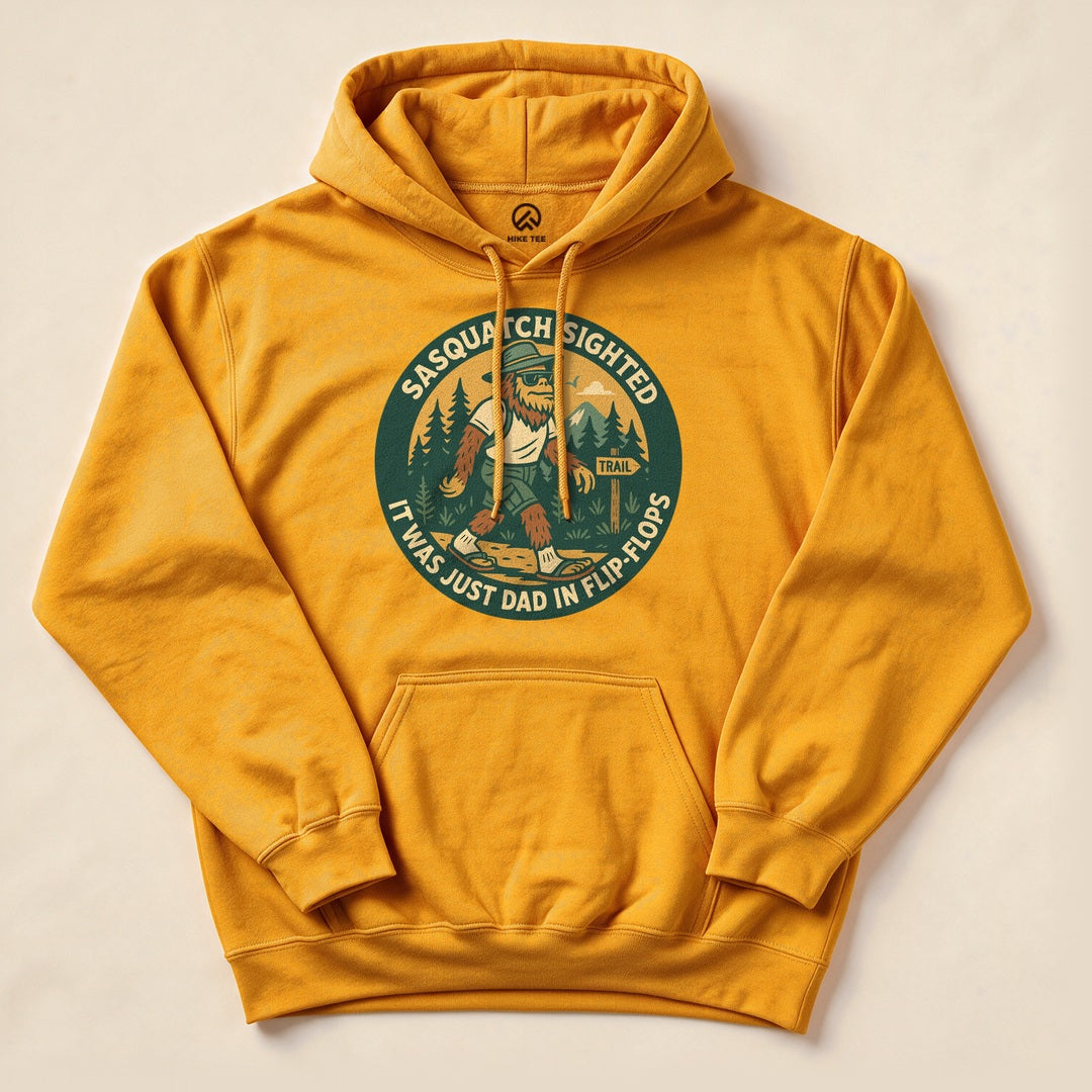 A yellow hoodie featuring the graphic "Sasquatch Sighted" with a humorous slogan reading "It was just Dad in flip flops.