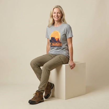 A woman sits on a cube wearing a graphic t-shirt featuring a sunset scene and the text "Badlands National Park Shirt.
