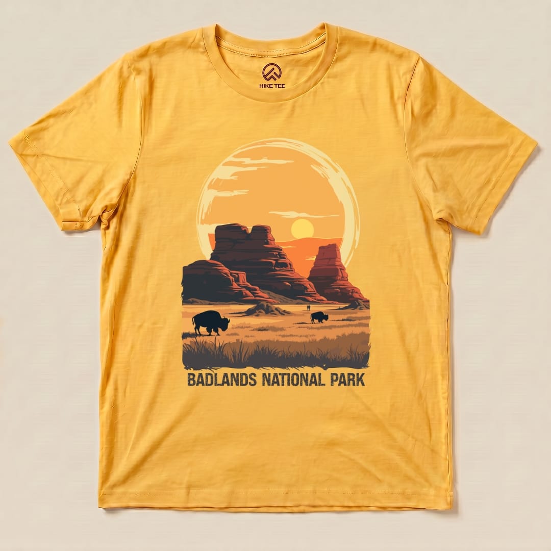 A graphic t-shirt featuring a sunset over Badlands National Park with bison and the words "BADLANDS NATIONAL PARK" printed below.