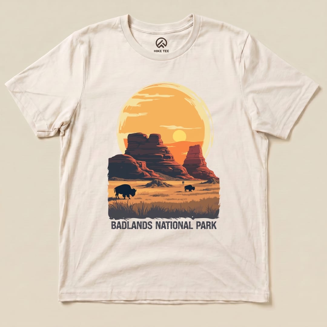 A graphic t-shirt featuring the text "BADLANDS NATIONAL PARK" alongside a sunset over rock formations and bison silhouettes.