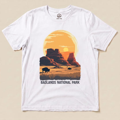 A graphic t-shirt featuring a sunset over Badlands National Park, with bison silhouettes and the words "BADLANDS NATIONAL PARK.