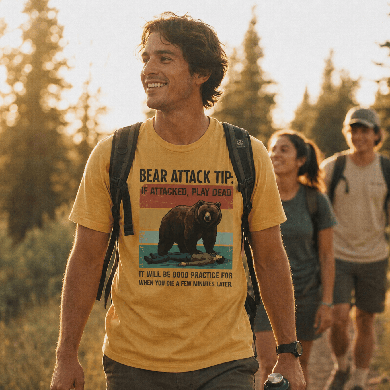 A man smiles while hiking in a sunlit forest, wearing a graphic t-shirt featuring the "Bear Attack Tip Retro Shirt" design with a bear and humorous advice.