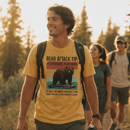 A man smiles while hiking in a sunlit forest, wearing a graphic t-shirt featuring the "Bear Attack Tip Retro Shirt" design with a bear and humorous advice.