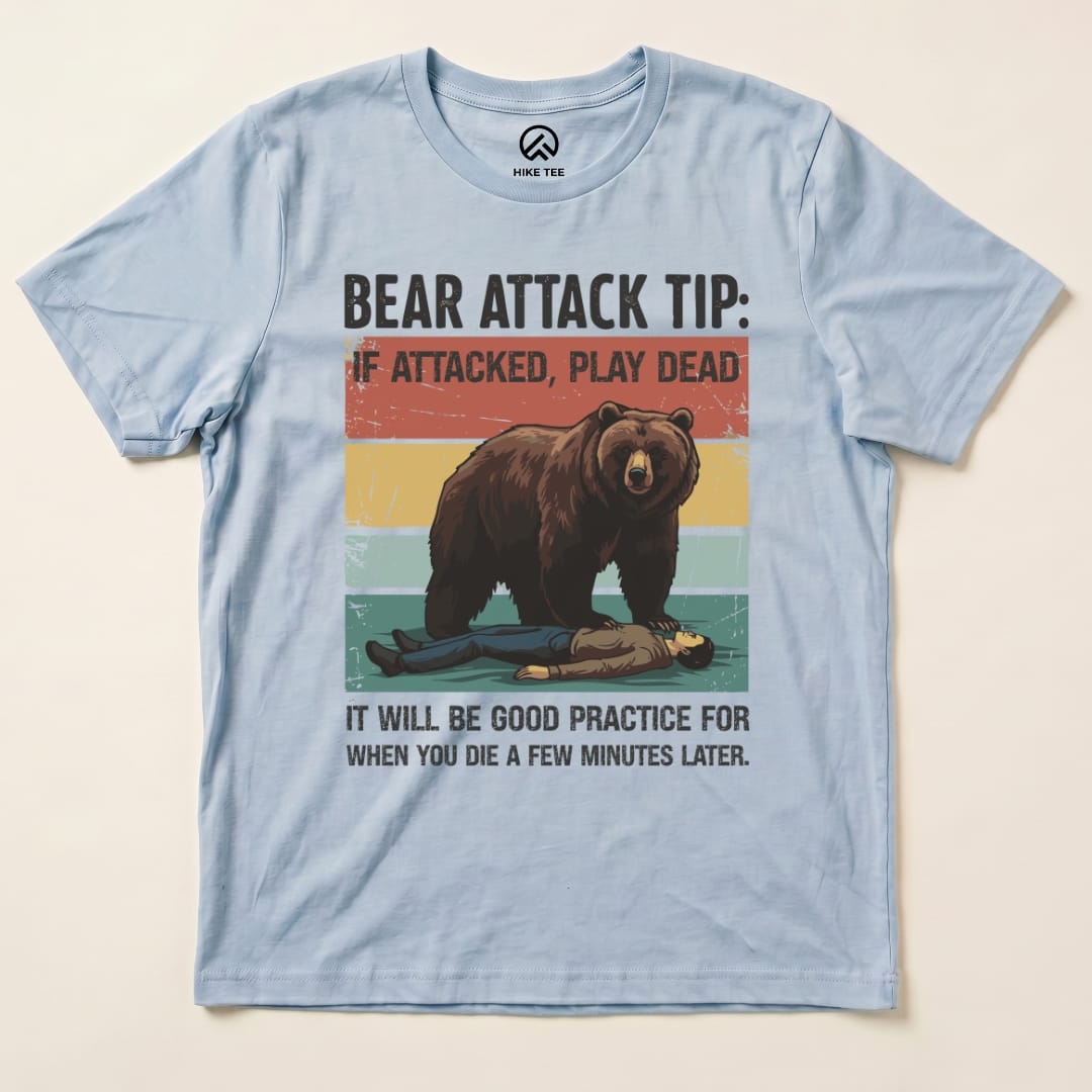 A light blue graphic t-shirt featuring a playful design of a bear and a person, labeled "Bear Attack Tip Retro Shirt.
