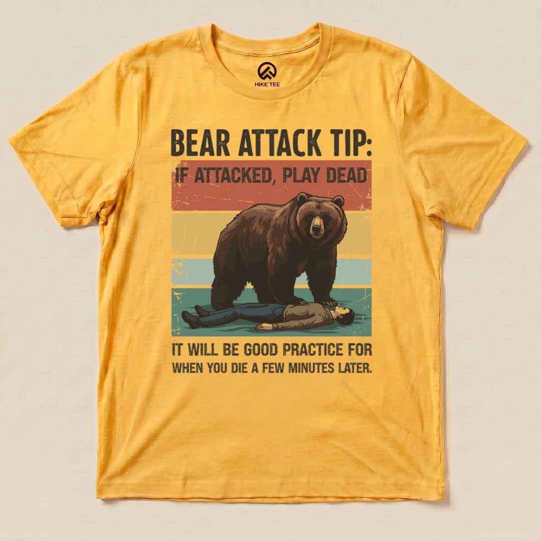 A yellow graphic t-shirt featuring a bear looming over a person with the text "Bear Attack Tip: If attacked, play dead. It will be good practice for when you die a few minutes later.