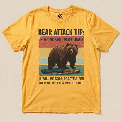 A yellow graphic t-shirt featuring a bear looming over a person with the text "Bear Attack Tip: If attacked, play dead. It will be good practice for when you die a few minutes later.
