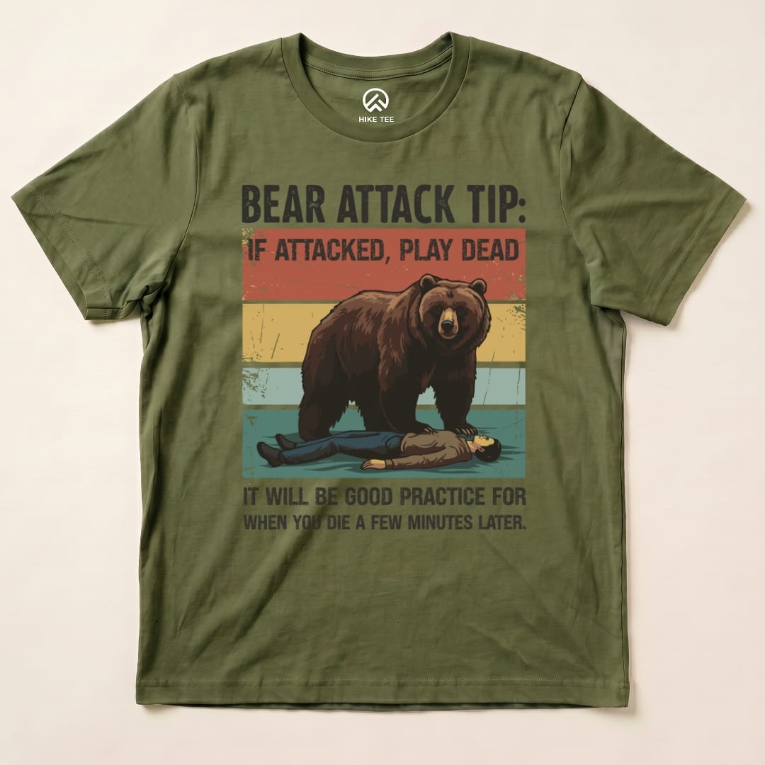 Graphic t-shirt featuring a humorous design of a bear and a person playing dead, with the text "Bear Attack Tip: If attacked, play dead.