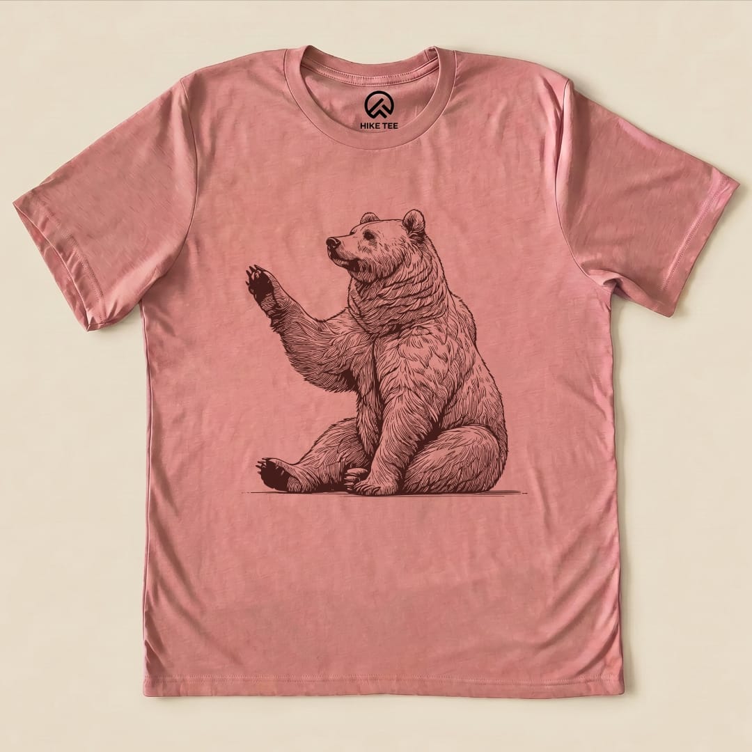 The "Bear is Watching Shirt" features a whimsical illustration of a waving bear, printed on a pink graphic t-shirt.