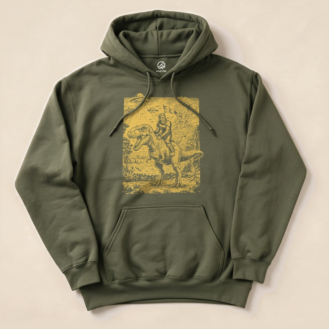 A graphic t-shirt featuring a humorous design of Bigfoot riding a dinosaur against a detailed backdrop, labeled "Bigfoot Dinosaur Hoodie.