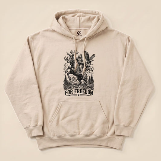 A beige "Bigfoot Moose Resist Hoodie" featuring a graphic of Bigfoot riding a moose with the slogan "FOR FREEDOM" below.