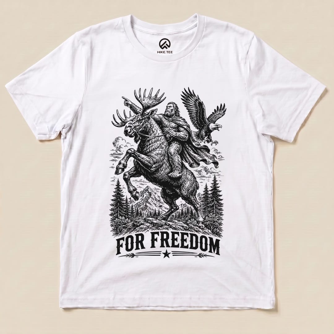 A graphic t-shirt featuring Bigfoot riding a moose with the slogan "FOR FREEDOM" beneath, showcasing a whimsical outdoor theme.