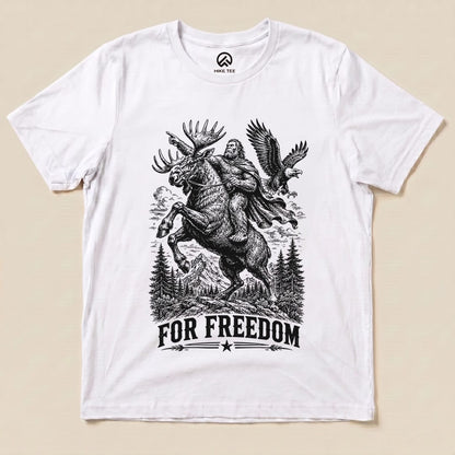 A graphic t-shirt featuring Bigfoot riding a moose with the slogan "FOR FREEDOM" beneath, showcasing a whimsical outdoor theme.
