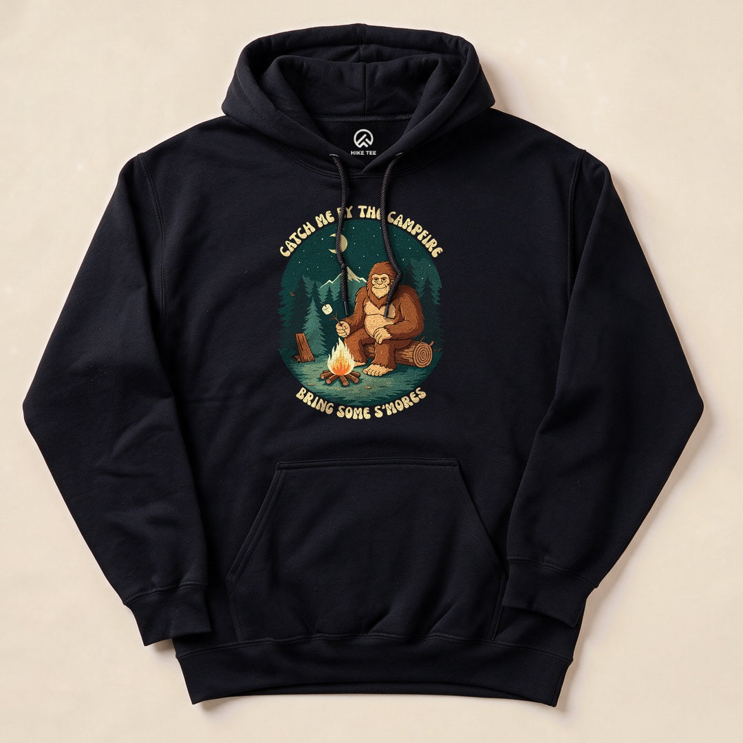 A navy hoodie featuring a graphic of a bear by a campfire with the text "Catch Me By The Campfire Bring Some S'mores.