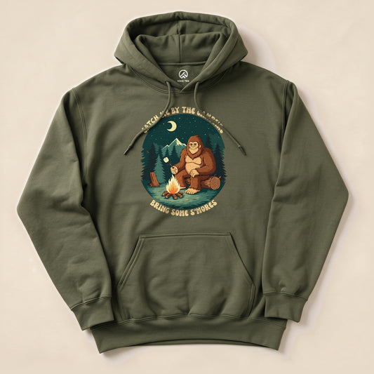 Olive green "Bring Some Smores Hoodie" featuring a graphic of Bigfoot roasting marshmallows by a campfire in a forest.