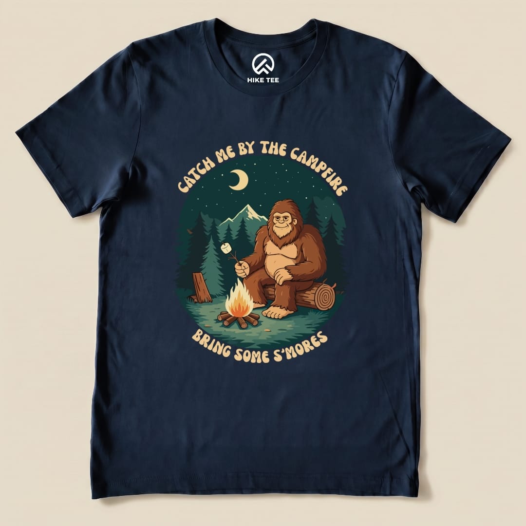 A navy graphic t-shirt featuring a bear-like creature by a campfire with the text "Catch Me by the Campfire Bring Some S'mores.