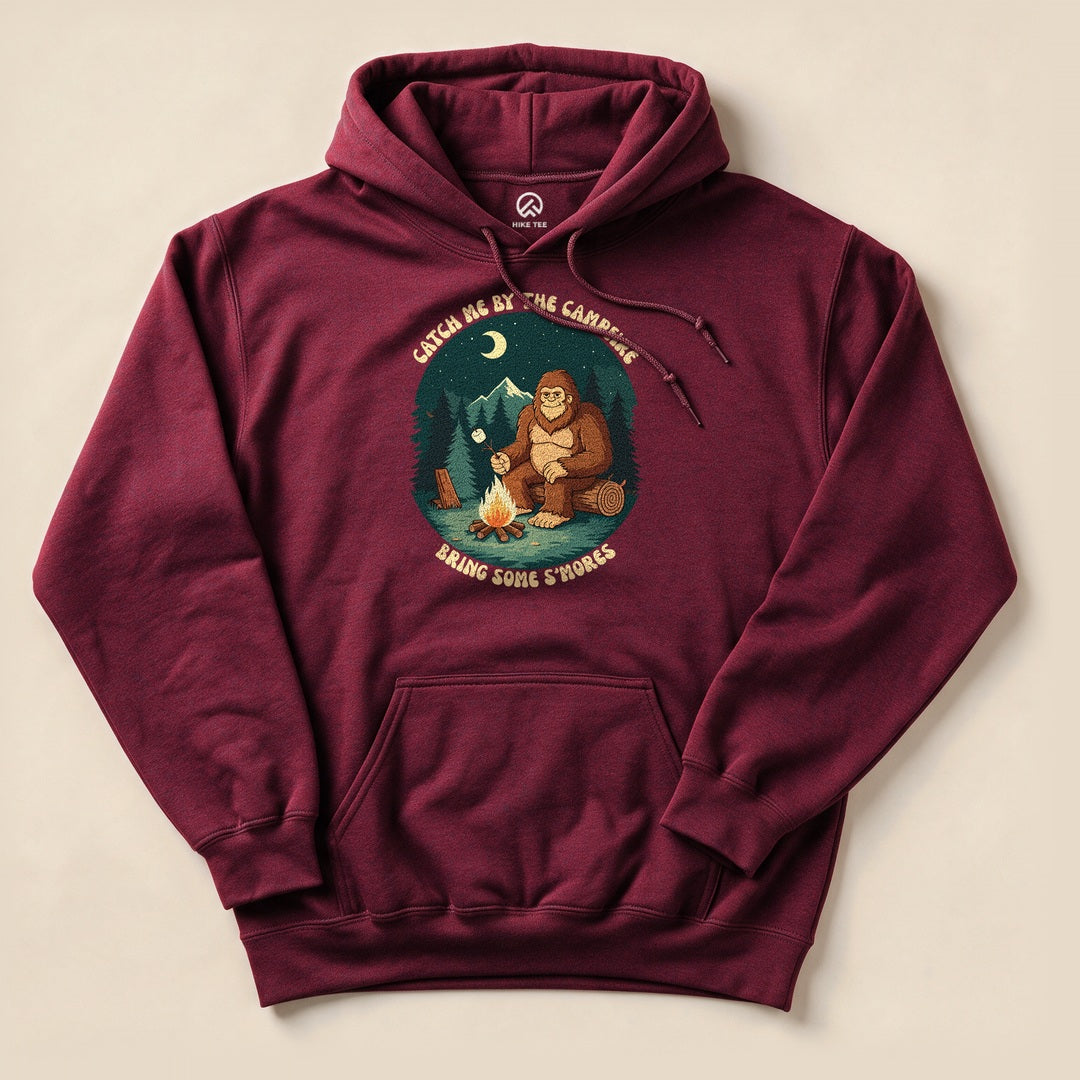 Graphic t-shirt "Bring Some Smores Hoodie" featuring a playful illustration of a bigfoot by a campfire with the text "Catch Me By The Campfire".