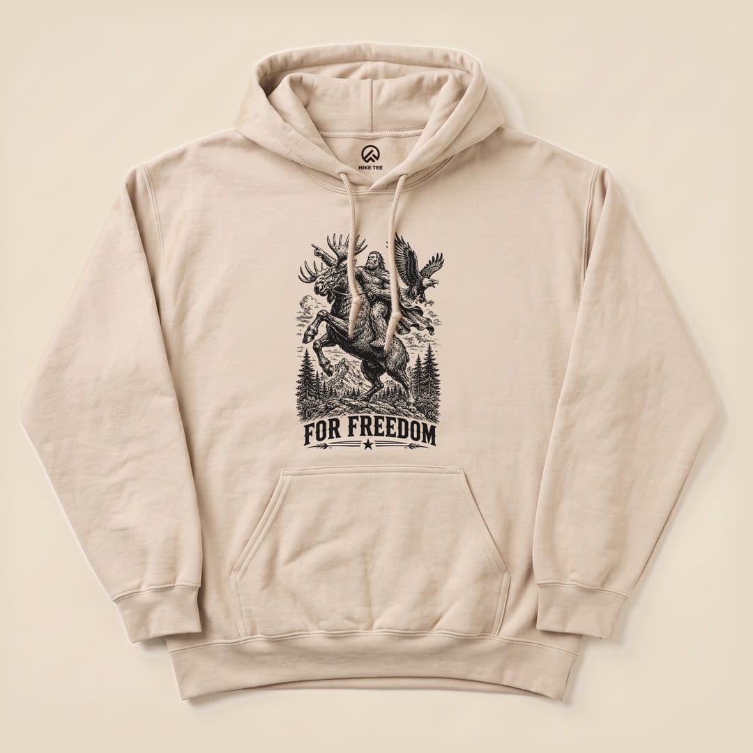 A beige "Bigfoot Moose Resist Hoodie" featuring a graphic of Bigfoot riding a moose with the slogan "FOR FREEDOM" below.