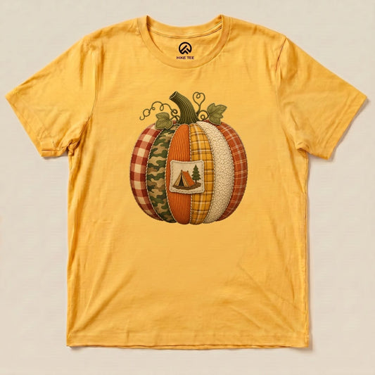 A graphic t-shirt in yellow featuring a colorful pumpkin design with various fabric patterns and a camping scene emblem, labeled "Camp Pumpkin Shirt.