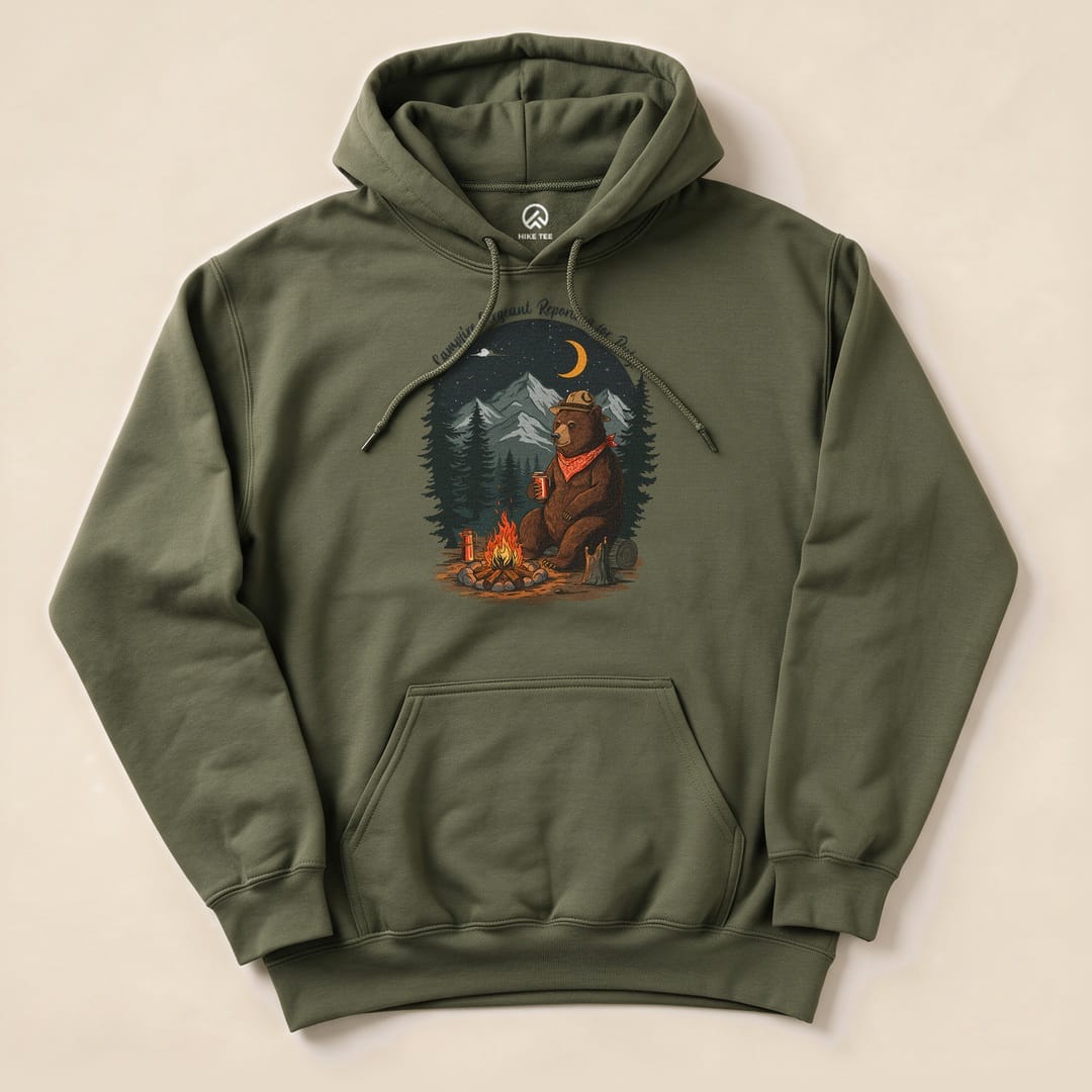 The Campfire Sergeant Bear Hoodie features a graphic of a bear in a hat sitting by a campfire surrounded by trees and mountains.