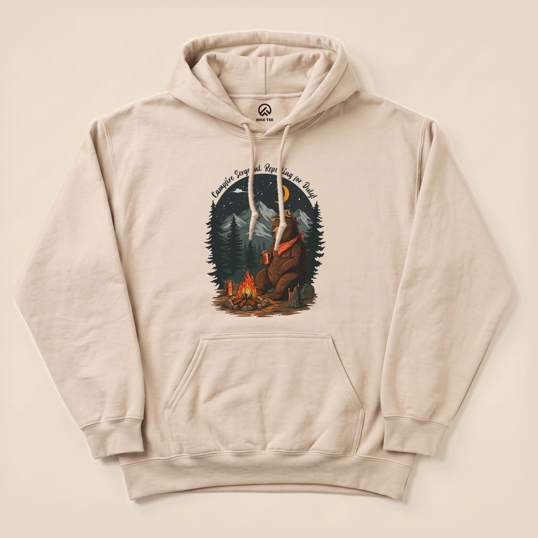 The Campfire Sergeant Bear Hoodie features a bear relaxing by a campfire, surrounded by trees, with a humorous slogan above.