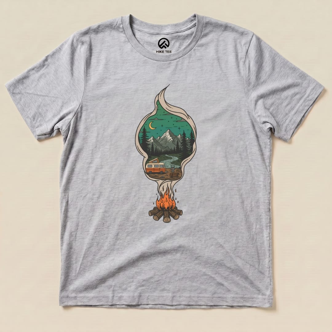 A graphic t-shirt featuring a campfire illustration with trees, mountains, and a camper, titled "Campfire Smoke Shirt.