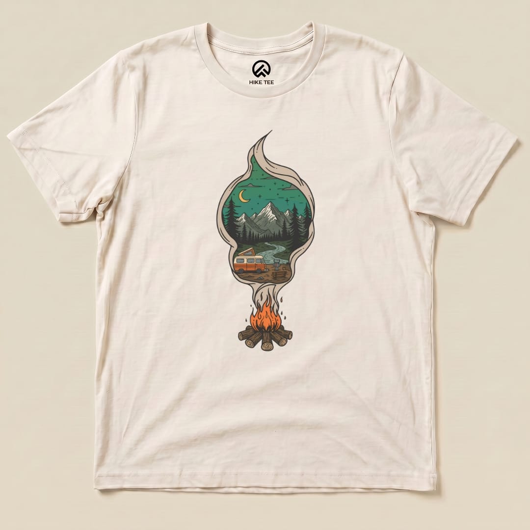 The Campfire Smoke Shirt features a whimsical graphic of a campfire with a tree and mountain scene inside smoke, set on a light-colored tee.