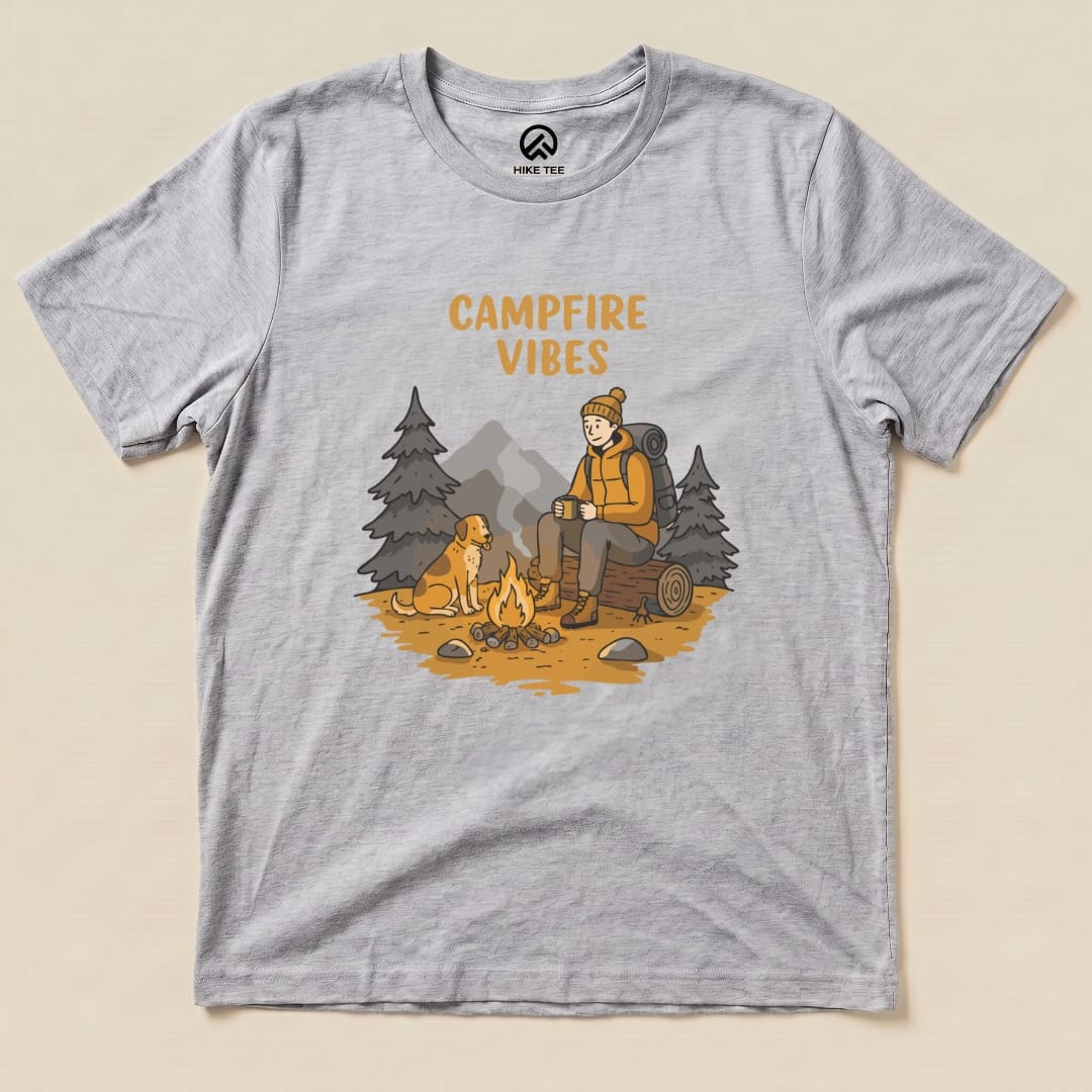 The Campfire Vibes Shirt features a cozy graphic of a person sitting by a campfire with a dog, surrounded by trees and mountains.