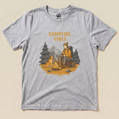 The Campfire Vibes Shirt features a cozy graphic of a person sitting by a campfire with a dog, surrounded by trees and mountains.