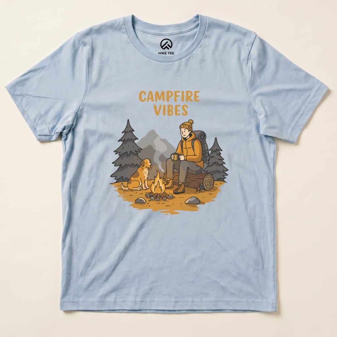 A light blue graphic t-shirt featuring the phrase "CAMPFIRE VIBES" and an illustration of a hiker sitting by a campfire with a dog.