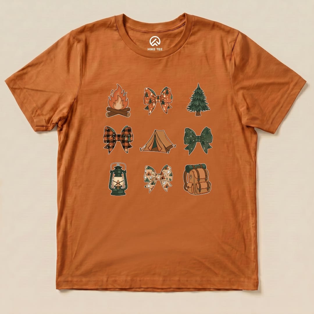 The Camping Bows Shirt features a fun graphic of camping icons, including bows, campfires, and lanterns, on an orange background.