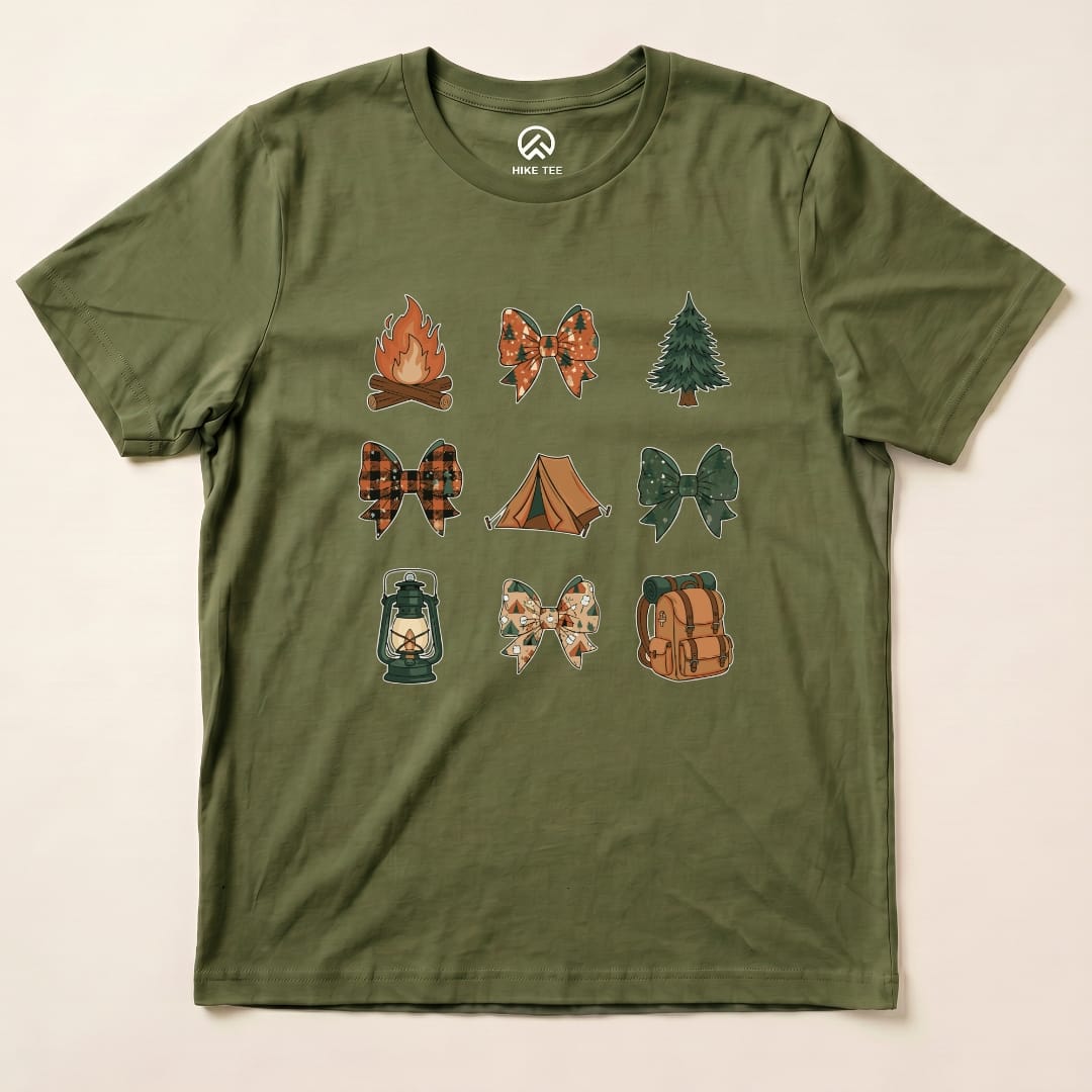 The Camping Bows Shirt features a whimsical design with various camping-themed bows and icons such as a campfire, tent, and lantern on an olive green graphic t-shirt.